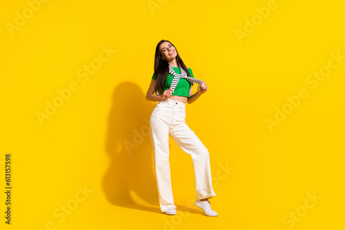 Full size portrait of nice cheerful young girl hands hold tied shoulders sweater posing isolated on yellow color background