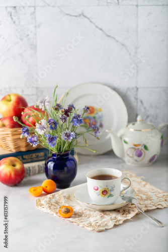 Summer still life: tea in a vintage cup, apricots, apples, books and cornflowers
