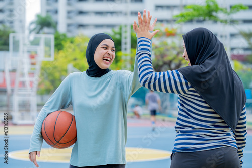 Tablou canvas Young asian muslim girl teen wearing hijab going to play basketball on the outdoor court in the morning with determination, Muslim sport concept