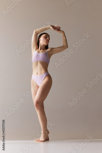 Full-length portrait of beautiful young girl with slim, fit body posing in underwear against grey studio background © Lustre