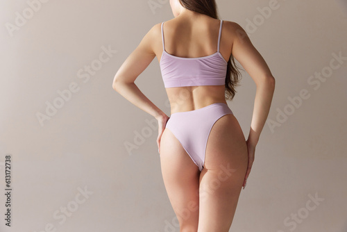 Cropped back view image of slim female body  back and buttocks. Model posing in underwear against grey studio background