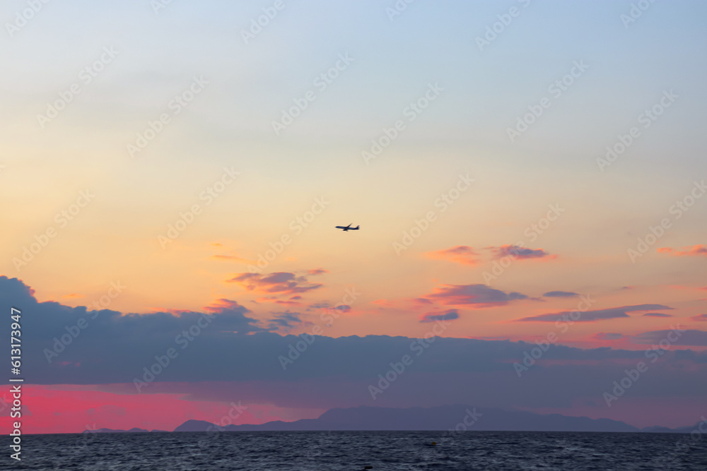 Single plane flying through the clouds at sunset at Paralia Ixia beach off Rhodes city 