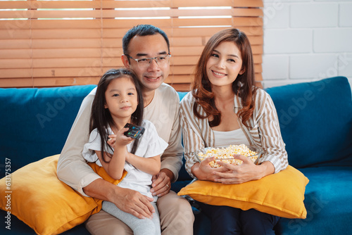 Asian Family consisting of parents  happy daughter watching TV or movie eating popcorn on sofa in living room at home. enjoy relaxing happiness.