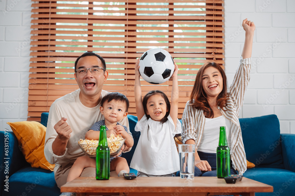 Asian Family with daughter watching sport football cheering excited eating popcorn on sofa in living room at home. enjoy relaxing happiness.