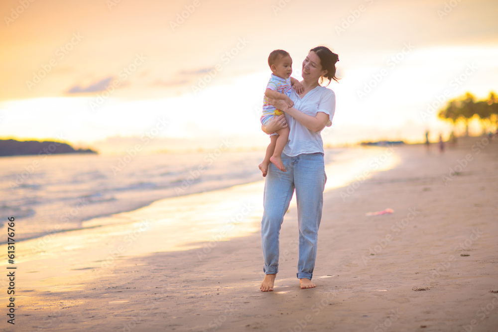 Mother and baby on tropical beach at sunset.