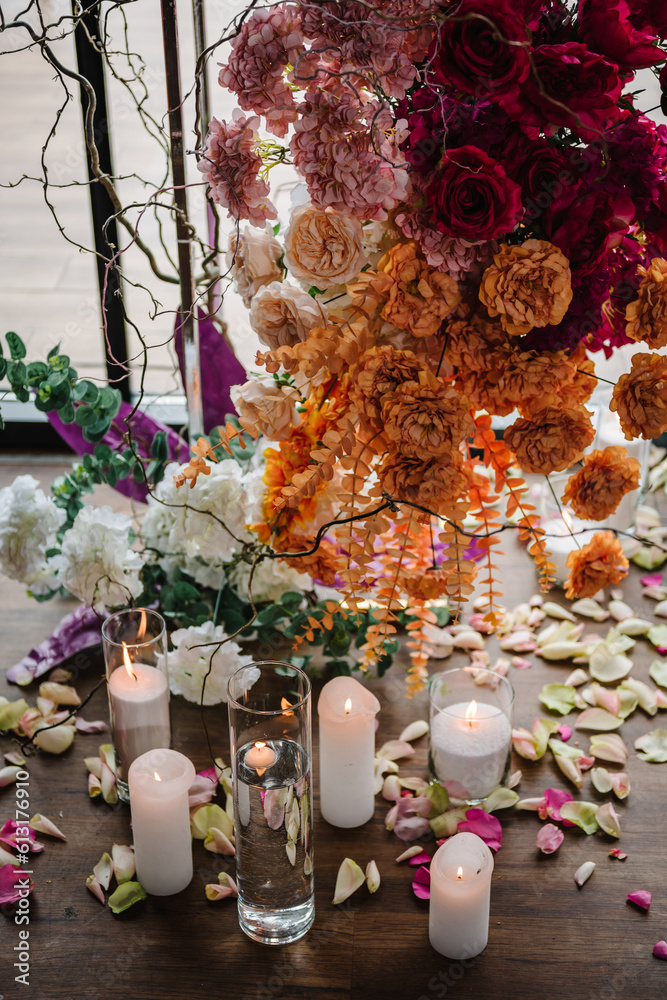 Candles, rose petals on floor. Closeup decor detail. Photo wall, arch decorated pink, orange flower for birthday party in banquet area, hall. Wedding reception for luxury ceremony. Decoration of event