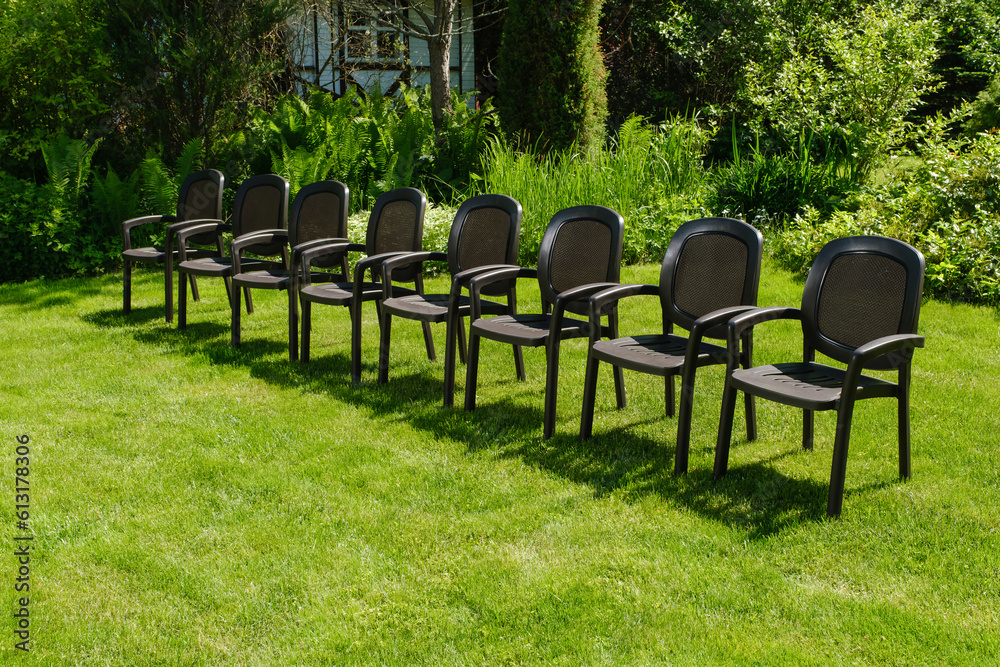 Dark brown chairs in green garden. Wet chairs on a green grass. Plastic chairs in ornamental garden background. Shallow depth of field