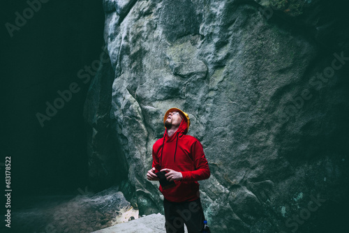 Young man tourist in dark mystery deep cave looking up at sunlight