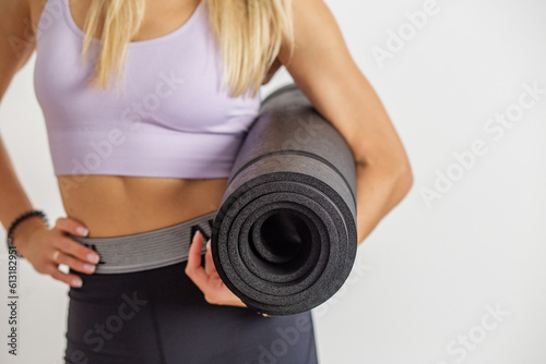 Girl with sports mat is preparing for workout. Woman with slim figure on white background. Close up