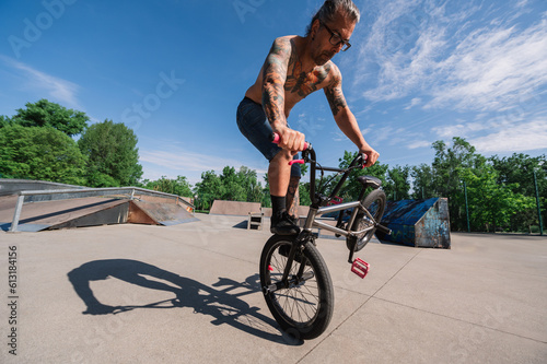 Wide angle view of an urban tattooed man doing tricks and stunts with his bmx in a skate park.