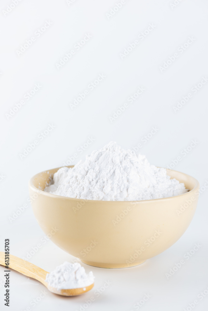 Tapioca starch in a bowl and wooden spoon on a light background.