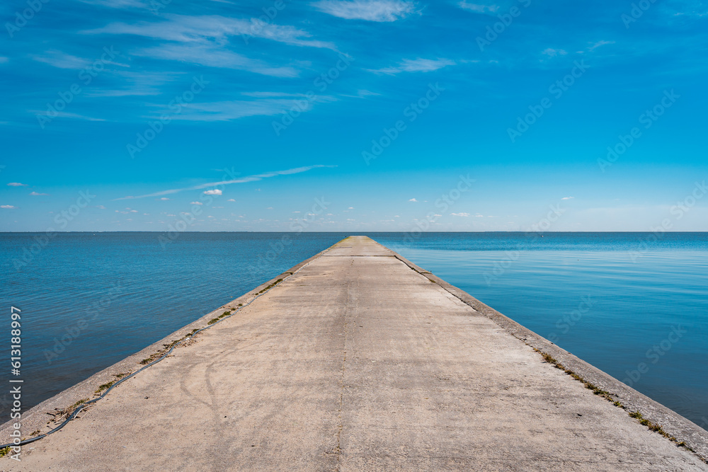 A long stone pier goes far into the sea against the background of a blue clear sky