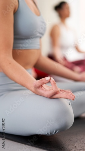 Unrecognizable young woman practicing yoga lesson sitting in Sukhasana posture with mudra gesture for mindfulness meditation. Group of people indoors doing the lotus position. Vertical photo.