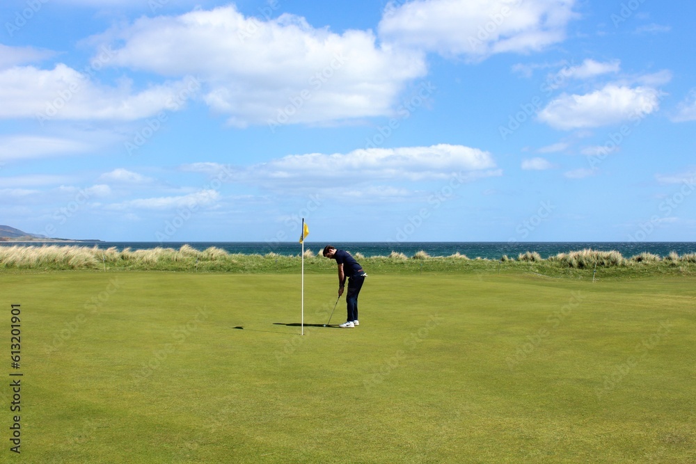 A man putting on a golf green on a links golf course with the ocean in the background on a beautiful sunny day in the highlands in Brora, Scotland A man putting on a golf green on a links golf course with the ocean in the background on a beautiful sunny day in the highlands in Brora, Scotland