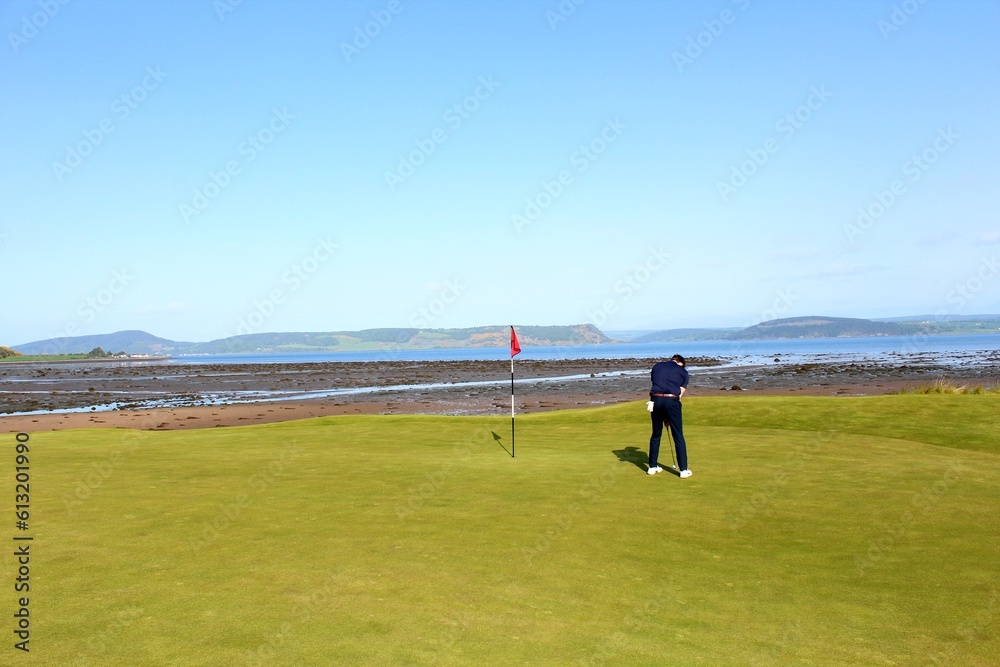 A man putting on a golf green on a links golf course with the ocean in the background on a beautiful sunny day in the highlands in Inverness, Scotland