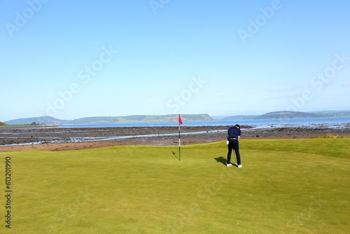 A man putting on a golf green on a links golf course with the ocean in the background on a beautiful sunny day in the highlands in Inverness, Scotland