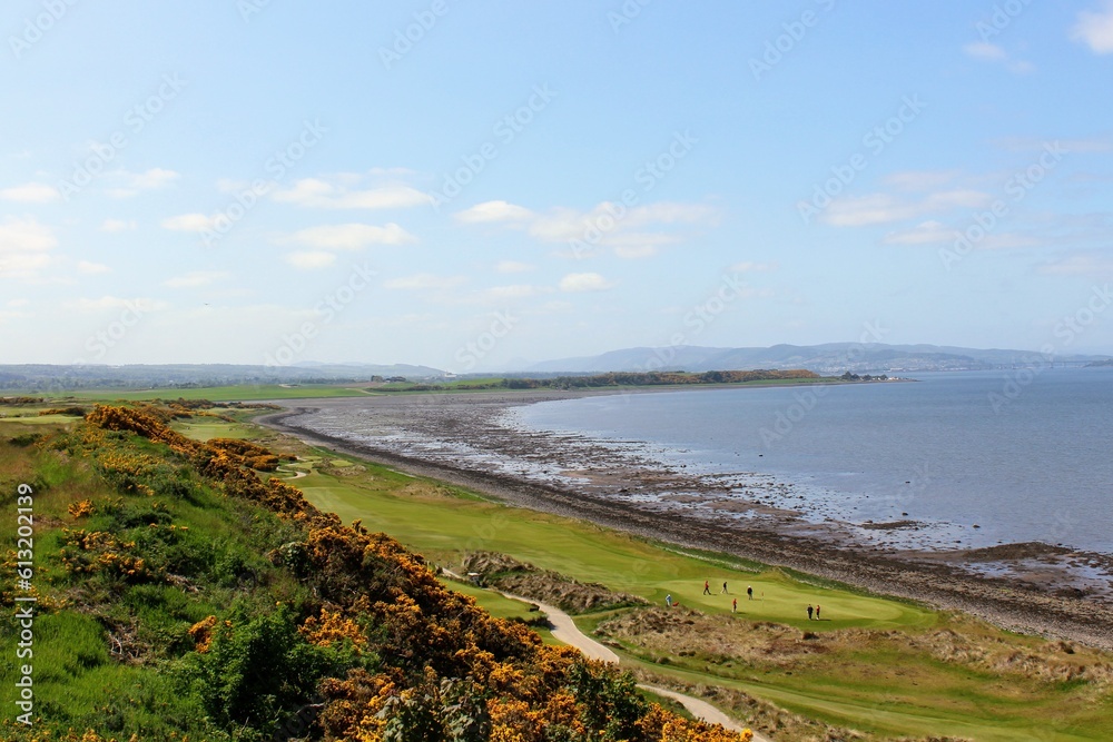 An incredible view of a golf hole in Scotland with the ocean in the background in Inverness, in the highlands of Scotland during spring with the gorse bush in full yellow bloom and beside the ocean An incredible view of a golf hole in Scotland with the ocean in the background in Inverness, in the highlands of Scotland during spring with the gorse bush in full yellow bloom and beside the ocean
