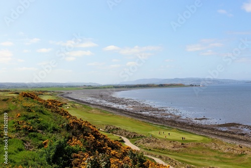 An incredible view of a golf hole in Scotland with the ocean in the background in Inverness, in the highlands of Scotland during spring with the gorse bush in full yellow bloom and beside the ocean