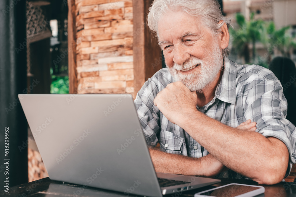 Active senior man using laptop sitting outdoor on a wooden table. Handsome bearded elderly businessman working online with wireless technology Active senior man using laptop sitting outdoor on a wooden table. Handsome bearded elderly businessman working online with wireless technology
