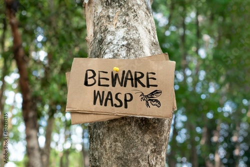 Beware Wasp on paper signpost sticked on tree the public park to warn people to avoid walking or running under trees which has wasp nest above, soft and selective focus.