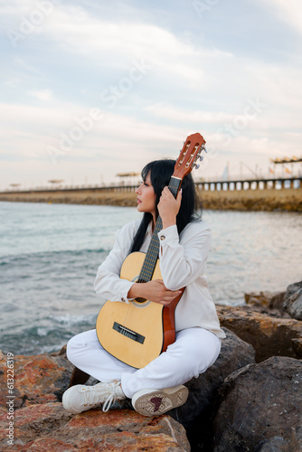 young girl with a guitar on the pier rocks in the sea (ID: 613226319)