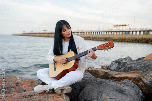 young girl with a guitar on the pier rocks in the sea (ID: 613226552)