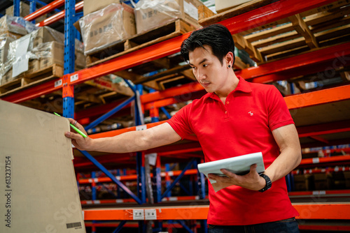 An Asian male worker inspects cardboard boxes in a large warehouse. distribution center Inventory management. warehouse, warehouse, industry