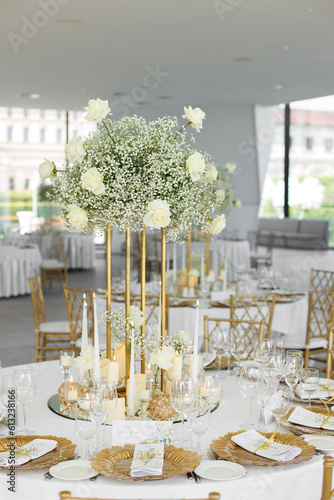 Served wedding tables with golden plates, decorative fresh  white roses and gypsophila flowers and different candles. Celebration details. Wedding decoration and decor, floristic concept	