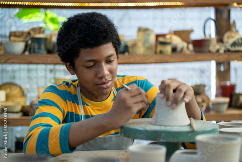 Konstfotografi In the workshop studio, a young African American boy proudly creates intricate clay pots and sculptures, his passion evident in the focused expression on his face
