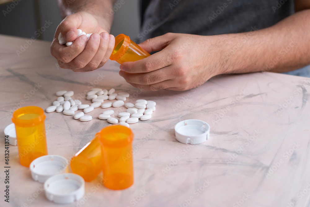 Close up of hand putting medicine drugs into a bottle of pills with many bottles and drugs on the table Close up of hand putting medicine drugs into a bottle of pills with many bottles and drugs on the table