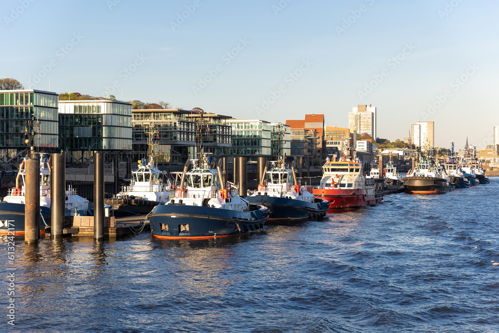 Many modern powerful tow ships service team mored in row at Hamburg Elbe harbour at evening sunset day time. Support tugboat vessel fleet in Germany industrial cargo freight harbor marine