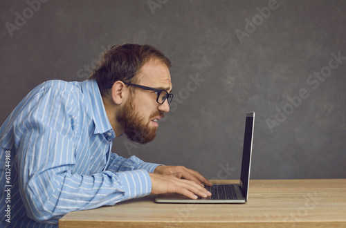 Side view close up of frustrated middle aged Caucasian man annoyed typing on laptop keyboard looking at screen. Crazy man sitting at a table and panicking at the message about a computer breakdown