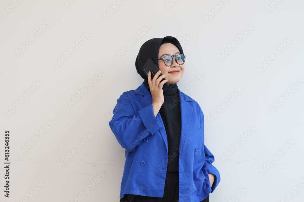 portrait of beautiful asian woman in hijab, glasses and wearing blue blazer making phone call and smiling portrait of beautiful asian woman in hijab, glasses and wearing blue blazer making phone call and smiling