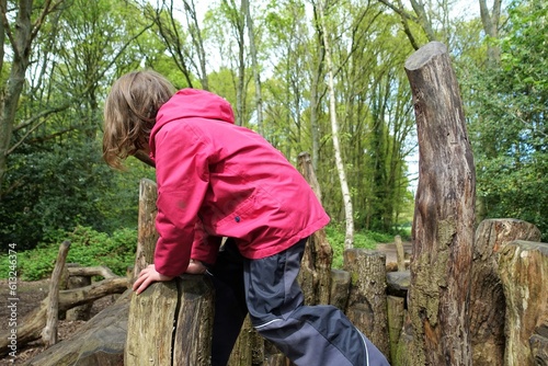 Child playing on natural woodland play area made with sustainably felled oak tree trunks on Chorleywood Common, Hertfordshire, England, UK