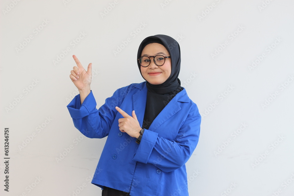 Beautiful young Asian Muslim woman in glasses, hijab and wearing blue blazer smiling confident and happy with both hands pointing up Beautiful young Asian Muslim woman in glasses, hijab and wearing blue blazer smiling confident and happy with both hands pointing up