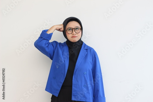 beautiful young Asian Muslim woman, wearing glasses and blue blazer with stressed expression while clenching fist on head
