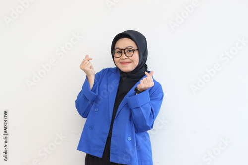 Beautiful young Asian Muslim woman, wearing glasses and blue blazer gesturing korean love sign while smiling