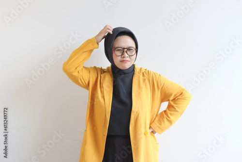 Beautiful young Asian Muslim woman, wearing glasses and yellow blazer showing stress gesture while holding head © Muchlis Nugroho