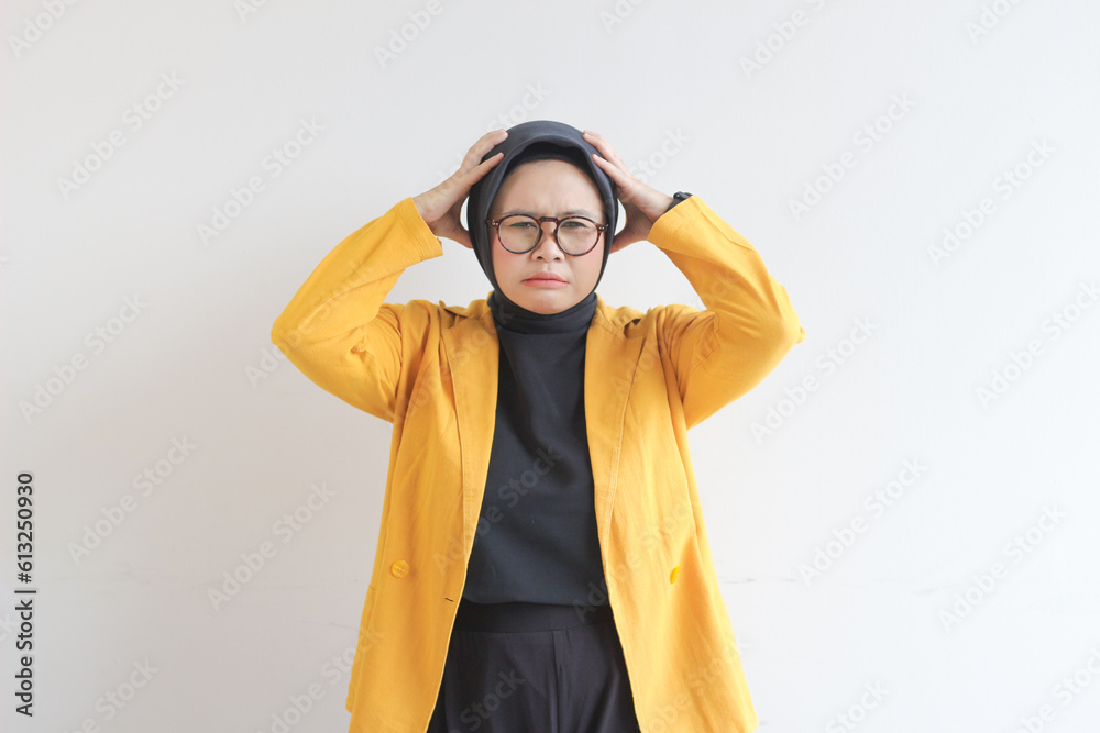 beautiful young Asian Muslim woman, wearing glasses and yellow blazer with dizzy expression holding head