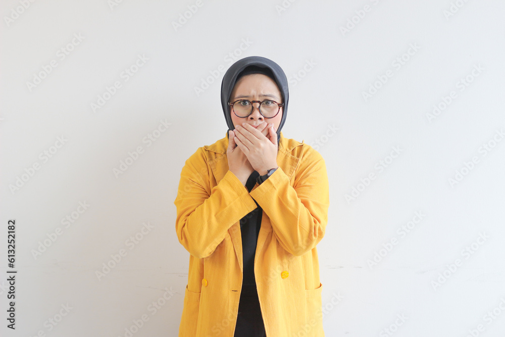beautiful young Asian Muslim woman, wearing glasses and yellow blazer with shocked expression while covering mouth beautiful young Asian Muslim woman, wearing glasses and yellow blazer with shocked expression while covering mouth