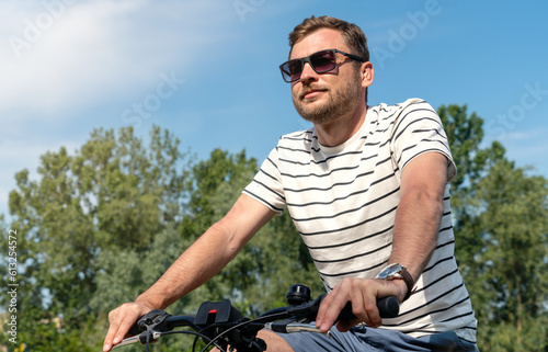Adult man wearing sunglasses riding a bicycle in the park at the weekend.