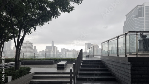 garden at rooftop during rainy day with higrise buildingof Bangkok, Thailand at the background. rooftop balcony with cityscape used as background. modern building's rooftop showing stairs and trees. photo