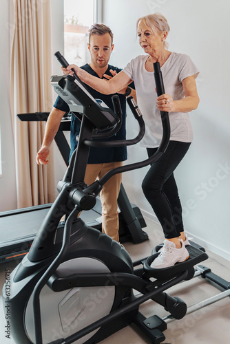 An elderly woman engages in a supervised exercise session at a clinic gym. With the guidance of a personal trainer or physiotherapist, she uses a step machine to improve her fitness and well-being.