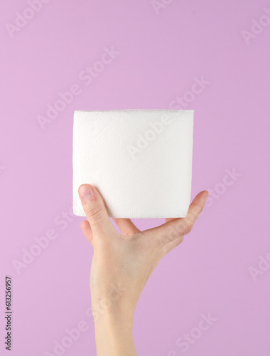 Hand holding a roll of white toilet paper on purple background