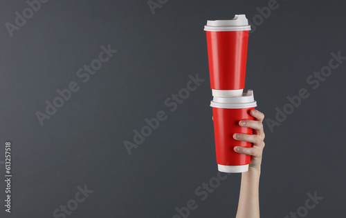 Female hand hold red disposable cups for hot drinks on a dark background