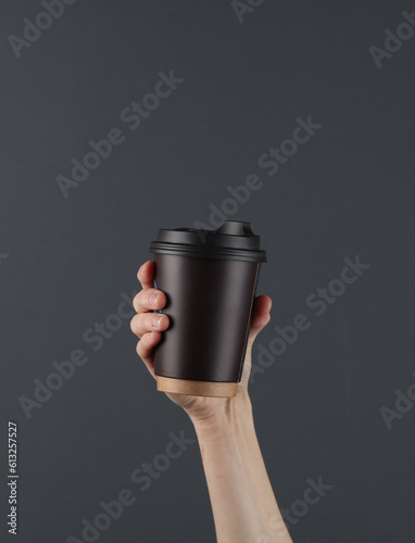 Female hand holding disposable cup for hot drinks on a dark background © splitov27