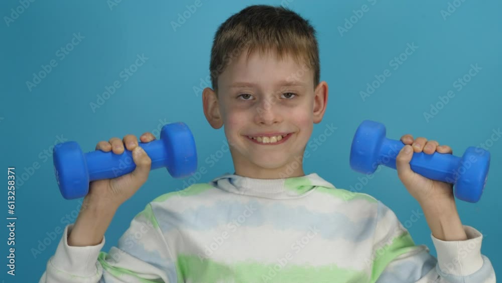handsome smiling caucasian boy 9 years old in casual clothes holds lifts up dumbbells, sports, studio shooting, blue background. handsome smiling caucasian boy 9 years old in casual clothes holds lifts up dumbbells, sports, studio shooting, blue background.