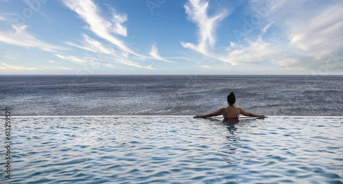 A woman lloking from the pool to the sea facing the sky photo