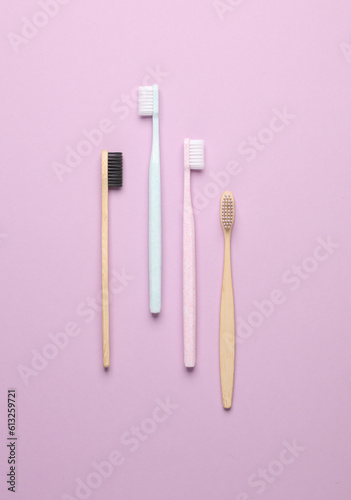 Plastic and eco bamboo toothbrushes on purple pastel background. Top view