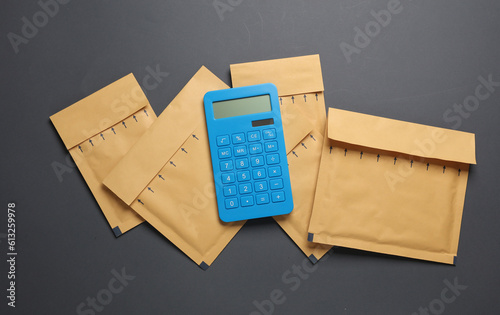 Parcel envelope and calculator on dark gray background. Delivery, Shipping cost calculation. Top view